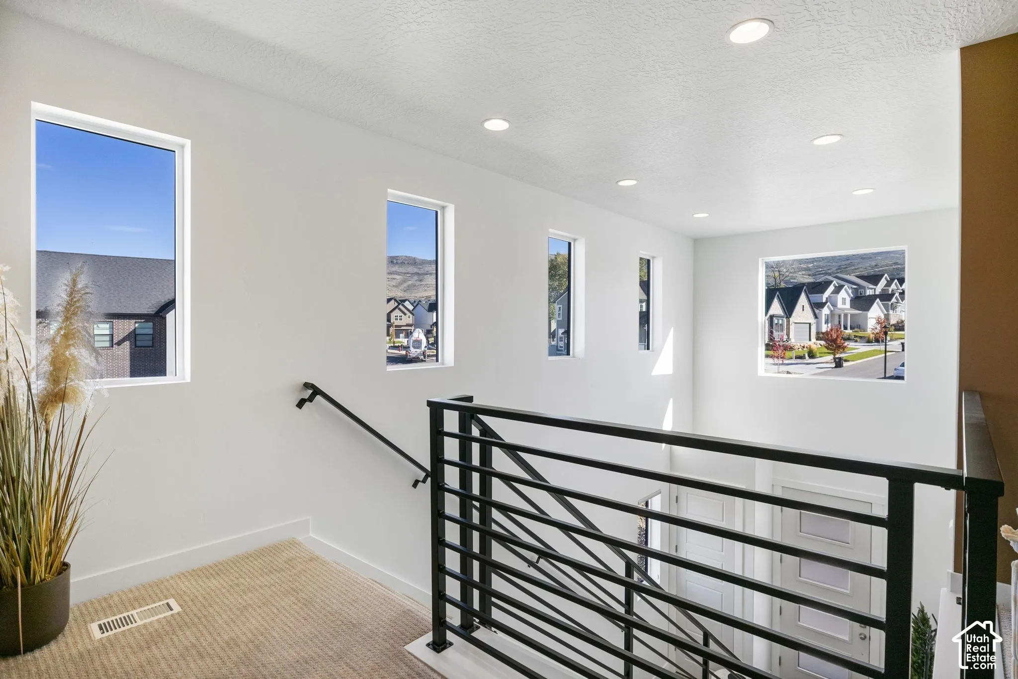 Upper landing featuring multiple windows, recessed lighting, white walls, and a black metal stair railing