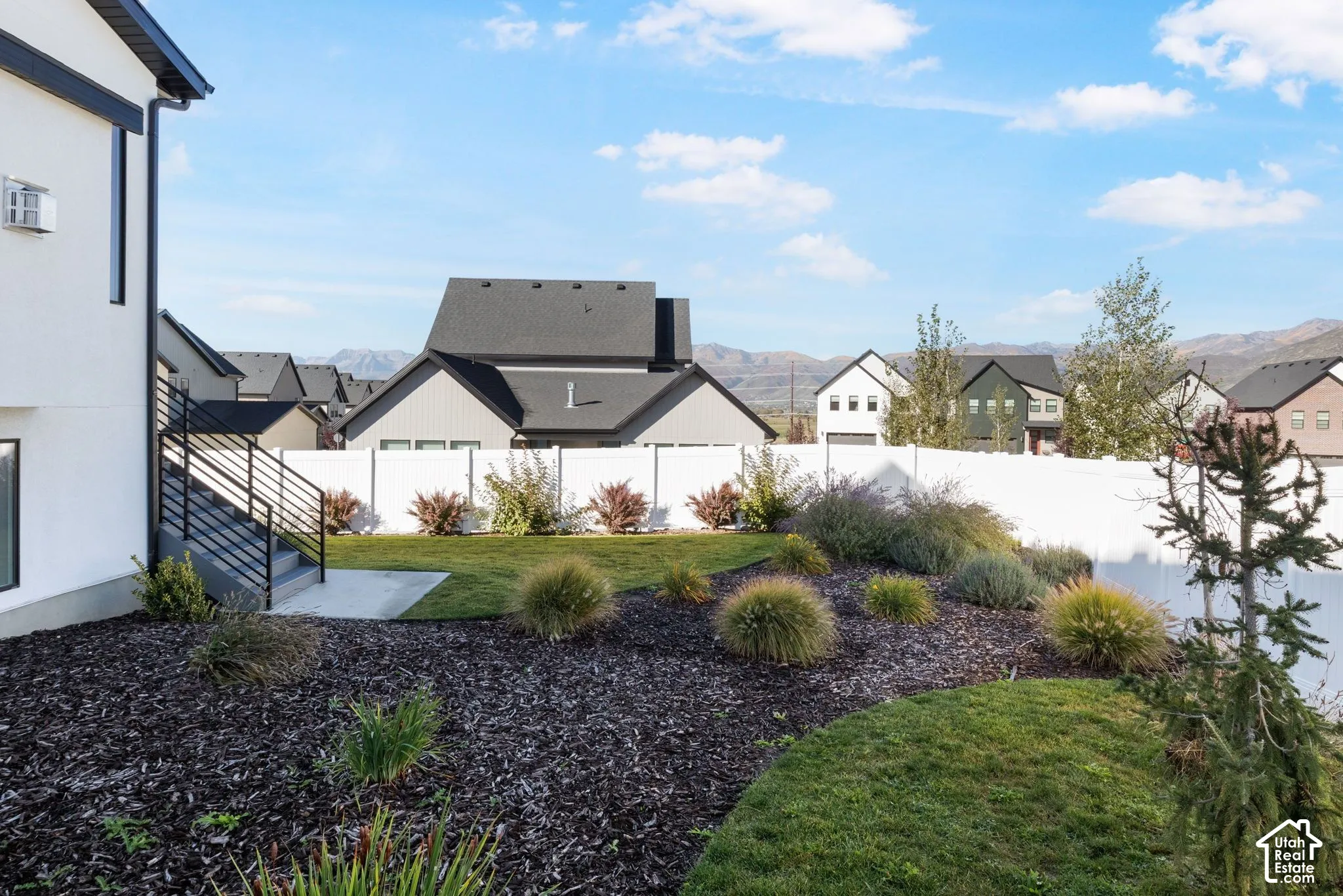 Landscaped yard featuring a white privacy fence, multi-level planting beds, and a concrete patio with black metal railings