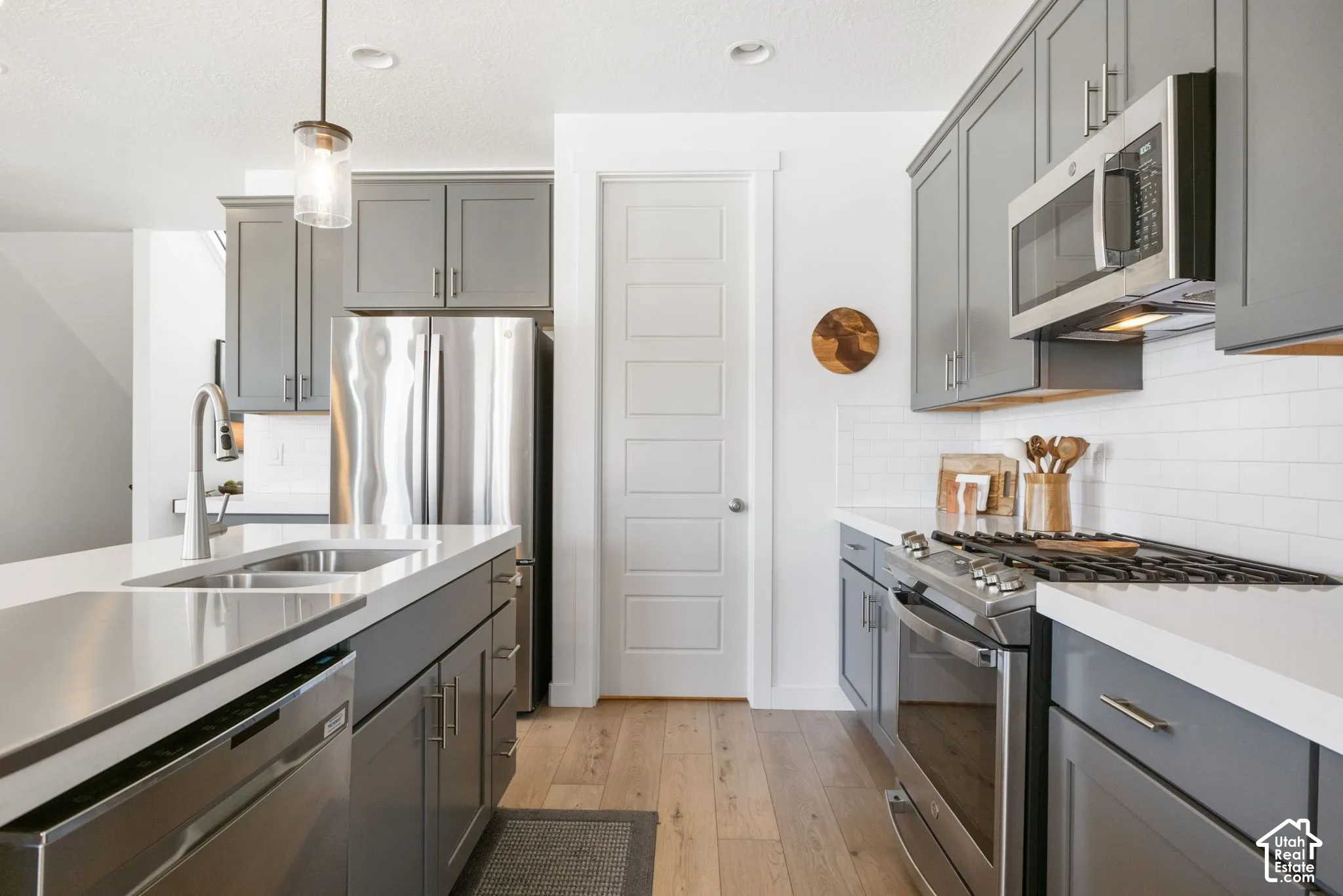 Kitchen featuring gray cabinetry, stainless steel appliances, a white subway tile backsplash, light-toned wood-finish flooring, and white countertops