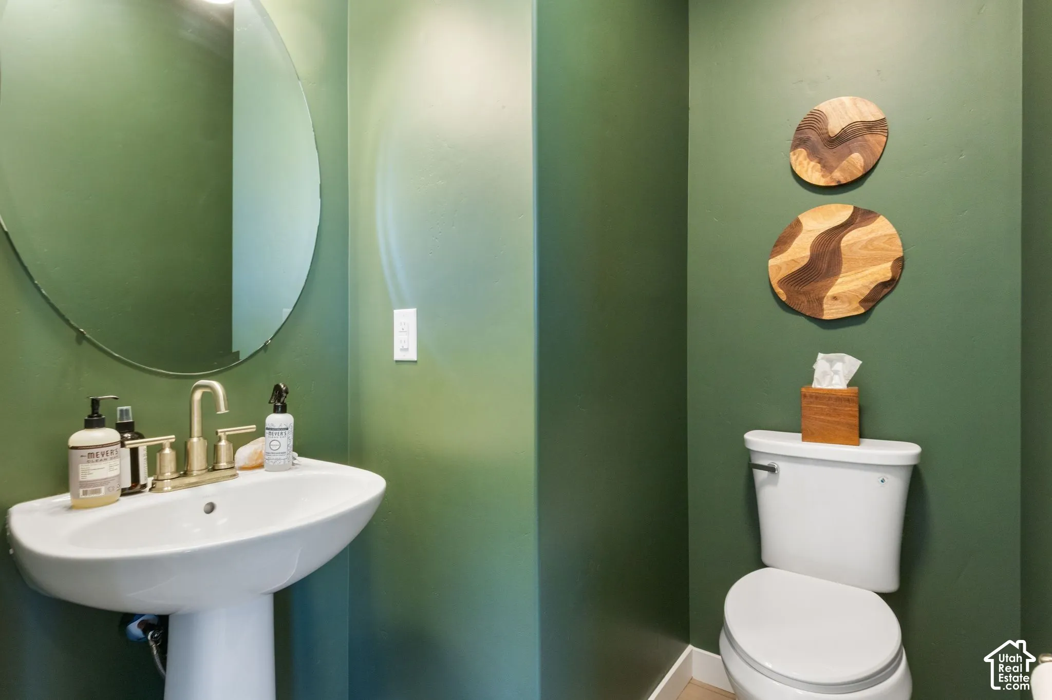 Pedestal sink with a polished brass faucet, oval mirror, and a white toilet