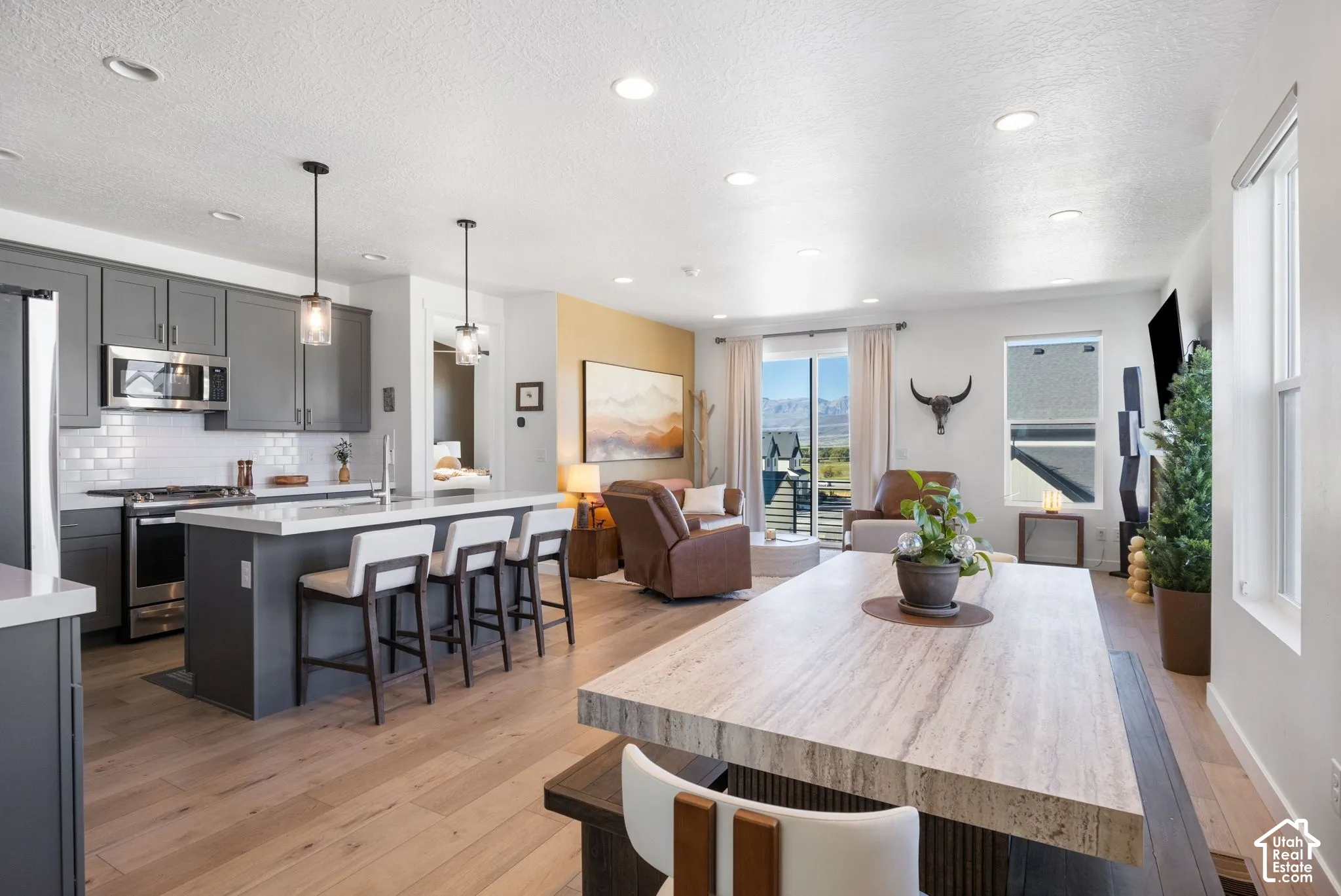 Open-concept interior featuring wood-finish flooring, a kitchen island with seating, stainless steel appliances, a white subway tile backsplash, and recessed lighting