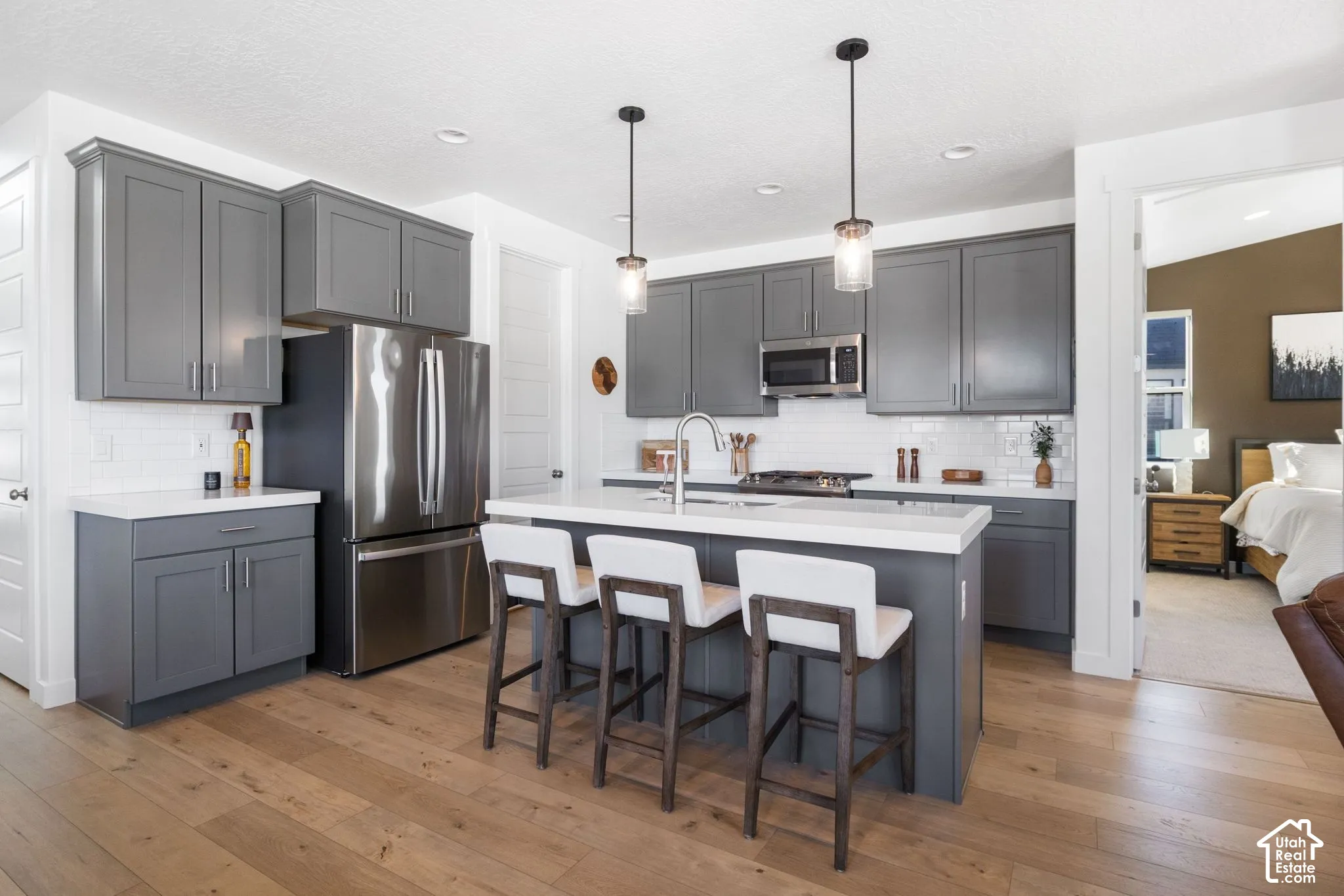 Wood-finish flooring, stainless steel appliances, grey cabinetry, white subway tile backsplash, and a kitchen island with pendant lighting