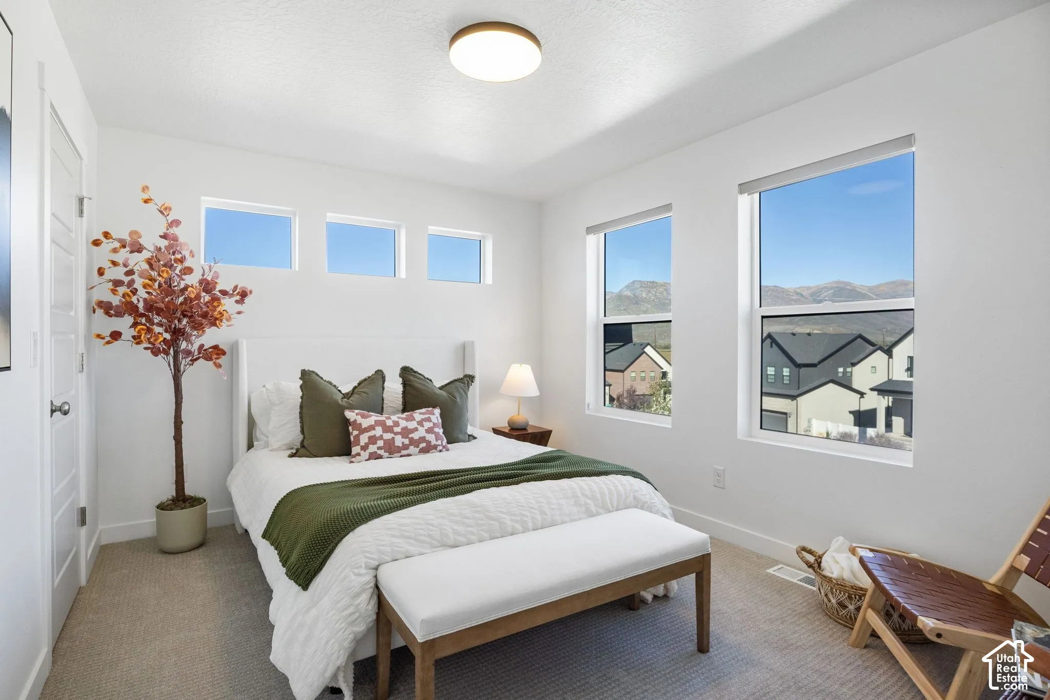 White walls and neutral carpeting, featuring a modern ceiling light fixture, and multiple windows