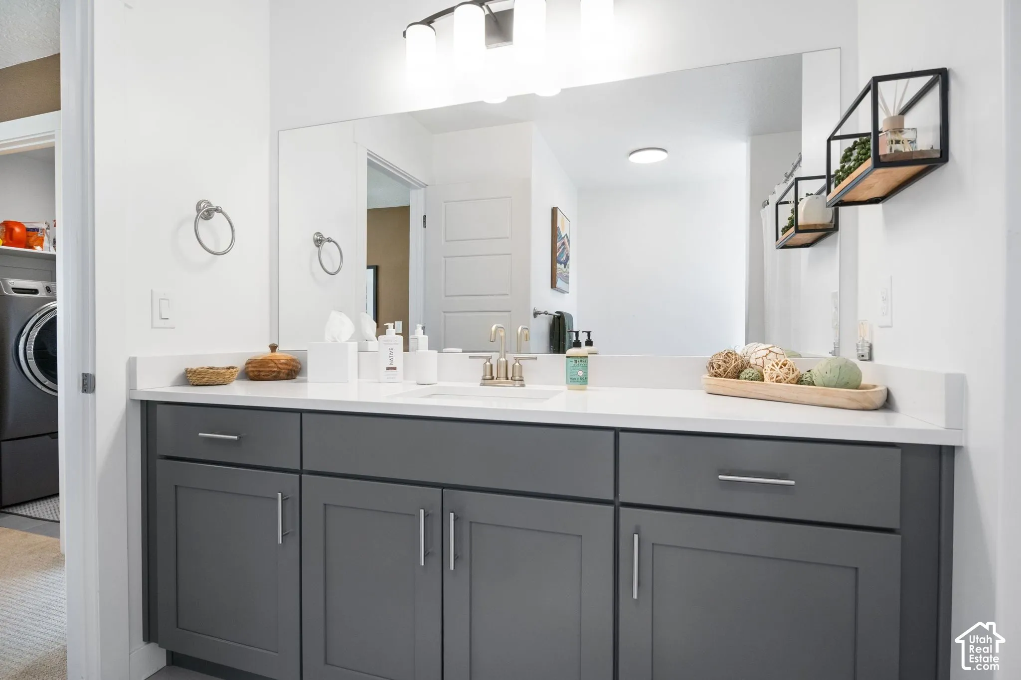 Gray cabinetry with brushed nickel hardware, expansive vanity mirror, and white countertop