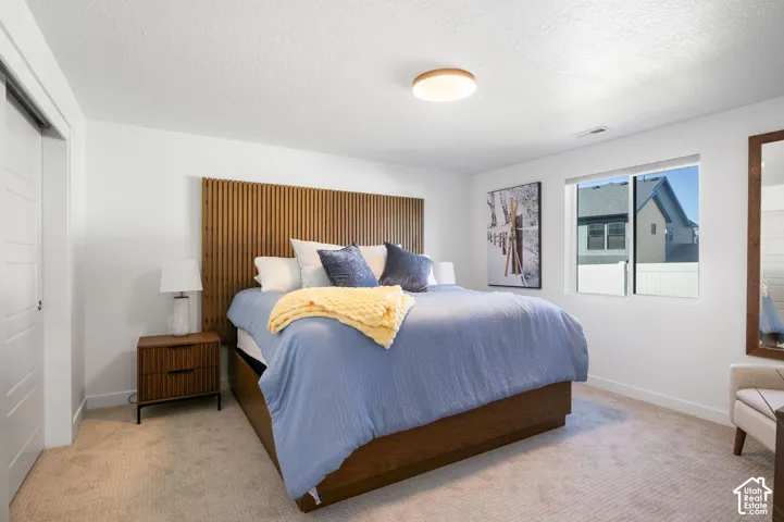 Built-in wooden headboard, large window, flush mount ceiling light, and carpeted flooring