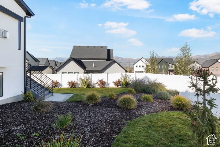Landscaped yard featuring a white privacy fence, multi-level planting beds, and a concrete patio with black metal railings