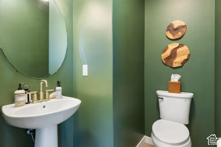 Pedestal sink with a polished brass faucet, oval mirror, and a white toilet