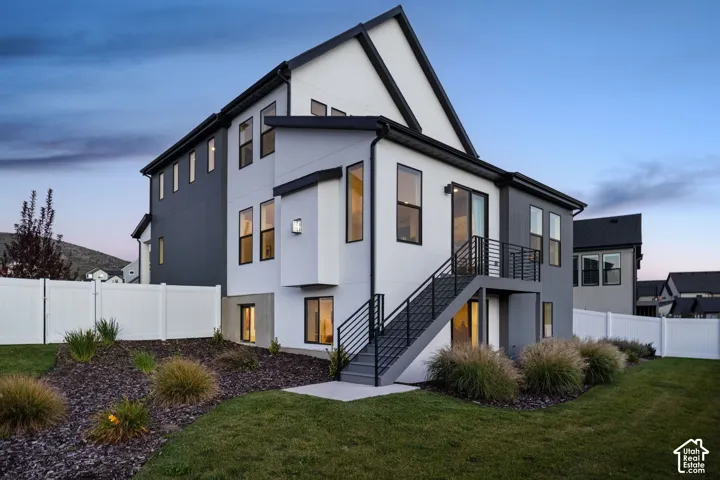 Modern exterior with black trim, multiple large windows, a two-story design, a balcony with metal railings, and a white privacy fence