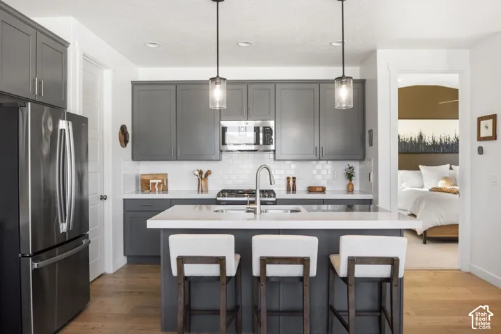 Kitchen featuring stainless steel appliances, grey cabinetry, a center island with a sink, white countertops, and a white subway tile backsplash