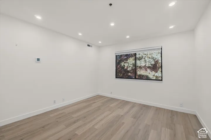 Recessed lighting, light wood-finish flooring, white walls, and a window with roller shade