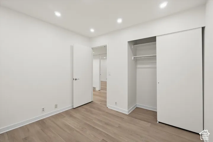 Recessed lighting, wood-finish flooring, sliding closet doors, and white walls