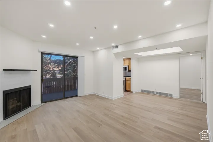 Recessed lighting, wood-finish flooring, sliding glass door, white subway tile fireplace surround, and a compact private balcony