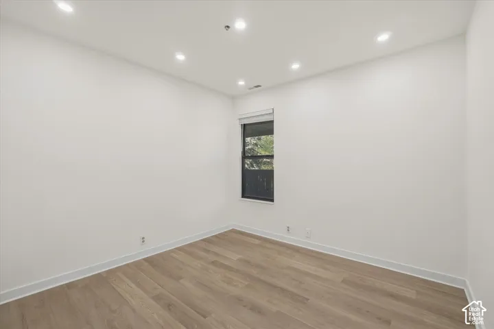Recessed lighting, wood-finish flooring, white walls, and a window with a roller shade