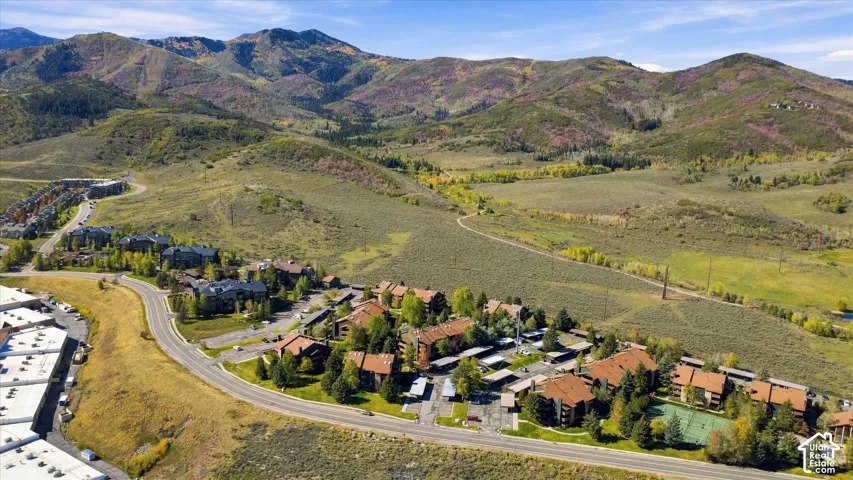 Mountainous terrain backdrop, residential buildings with brown roofs, paved roads, and a tennis court