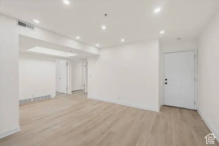 Recessed lighting, wood-finish flooring, white walls, white doors, and a skylight feature