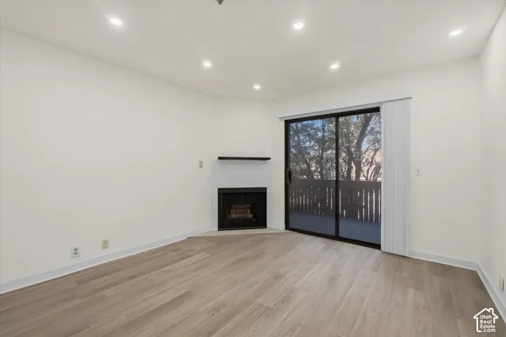 Light wood-finish flooring, recessed ceiling lighting, a corner fireplace with a subway tile surround, and a sliding glass door to an outdoor balcony