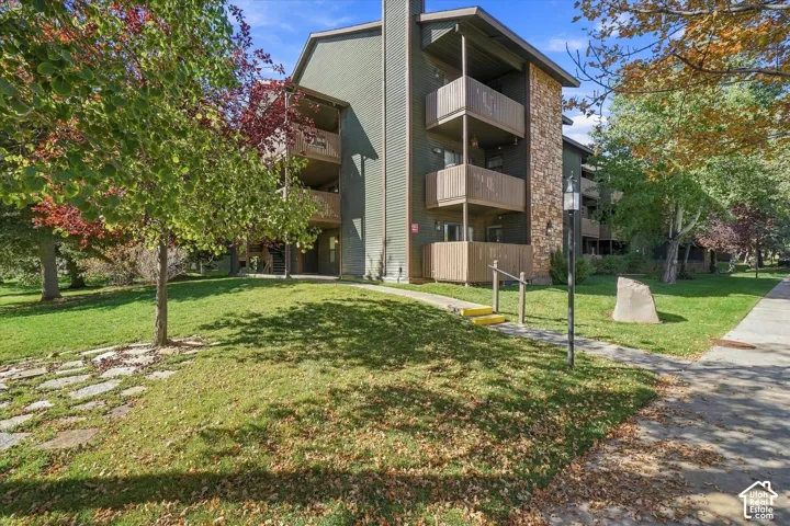 Multi-story building featuring stacked balconies, stone veneer accents, siding exterior, and a well-maintained lawn