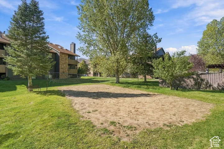 Sand court with net, surrounded by a grassy area and mature trees