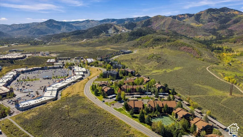 Expansive mountain terrain with varied vegetation, a paved road, a commercial center with ample parking, and residential structures featuring brown roofs