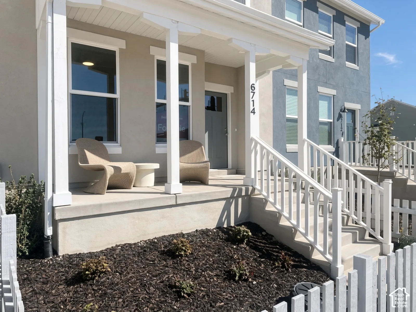 Covered front porch with white columns, concrete steps, and a white picket fence