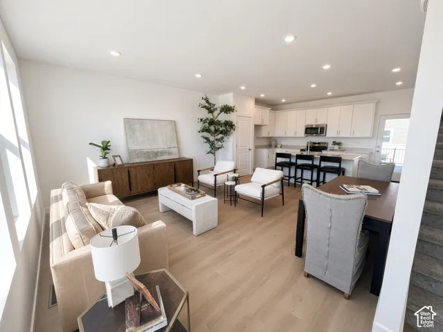 Open-concept living space featuring wood-finish flooring, recessed lighting, and a white kitchen with stainless steel appliances