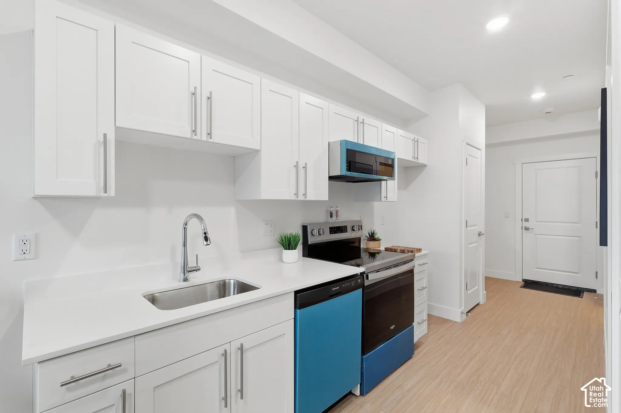 Kitchen featuring white shaker-style cabinetry, stainless steel sink with gooseneck faucet, light-toned wood-finish flooring, and a stainless steel appliance suite