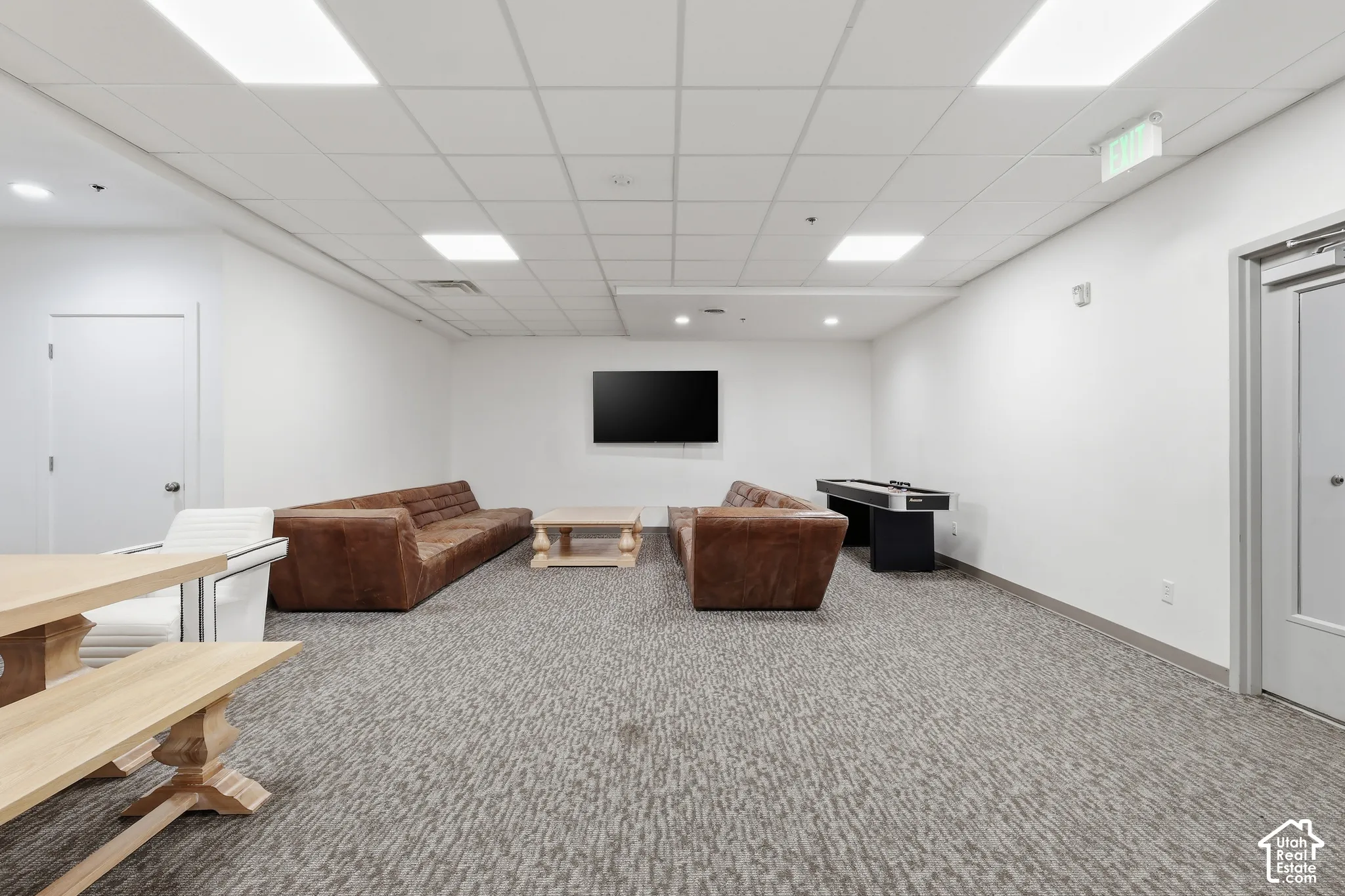 Spacious room featuring a textured carpet, white walls, and a dropped ceiling with recessed lighting