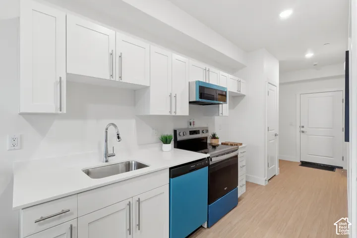 Kitchen featuring white shaker-style cabinetry, stainless steel sink with gooseneck faucet, light-toned wood-finish flooring, and a stainless steel appliance suite