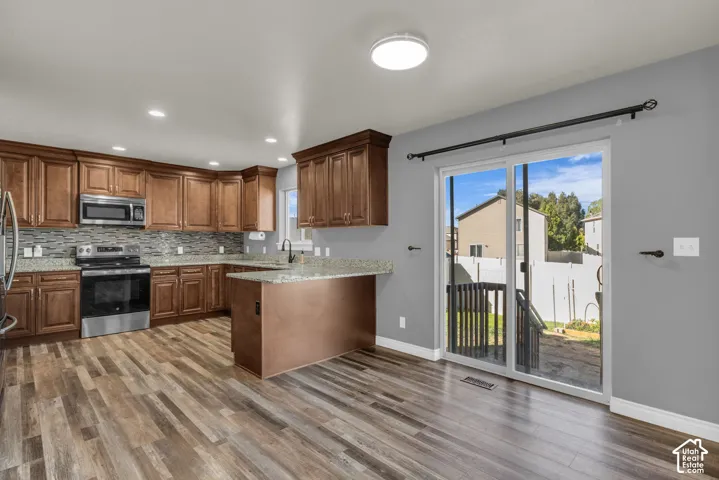 Wood-finish flooring, stainless steel appliances, granite countertops, tile backsplash, and sliding glass door