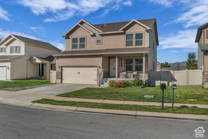 Two-story residence featuring a stucco exterior, an attached garage, a covered front porch, a well-maintained lawn, and a light-toned privacy fence