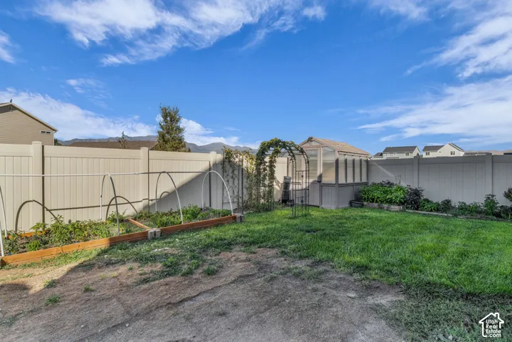 Expansive backyard featuring a greenhouse, arched trellis, raised garden beds, and perimeter fencing