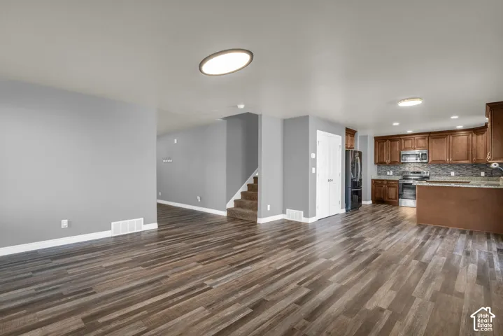Open-concept living area featuring wood-finish flooring, a kitchen with rich wood cabinetry, stainless steel appliances, and a tiled backsplash
