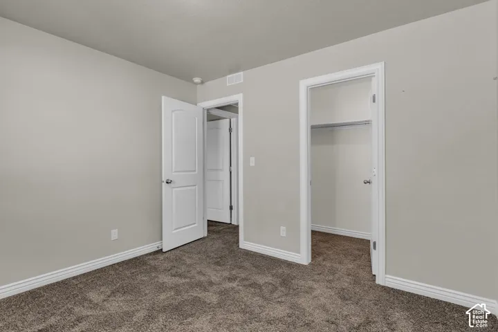 Neutral tone wall paint, textured carpet flooring, white trim, and a built-in closet with shelving