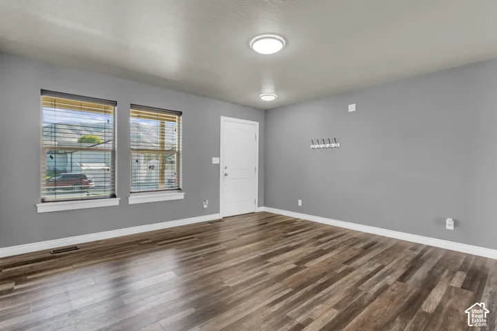 Wood-finish flooring, two large windows with blinds, flush-mount lighting, and a white paneled door