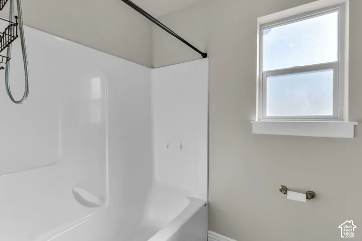 Integrated bathtub and shower unit with a black shower rod, white framed window, and a wall-mounted toilet paper holder