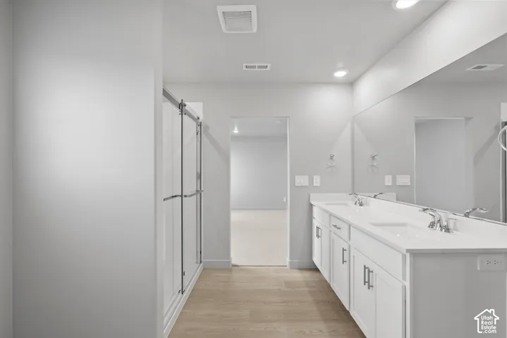 **DISLCAIMER**  Interiors do not show upgrades included. Dual vanity with white cabinetry, wood-finish flooring, and a glass-enclosed shower