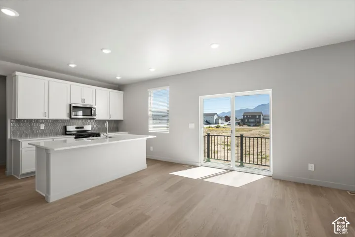 **DISLCAIMER**  Interiors do not show upgrades included. Open-concept kitchen with white cabinetry and an island, stainless steel appliances, wood-finish flooring, and sliding glass door with balcony