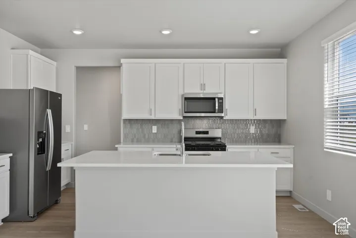 **DISLCAIMER**  Interiors do not show upgrades included. Kitchen featuring white cabinetry, a large kitchen island with a sink, stainless steel appliances, a tiled backsplash, and recessed lighting