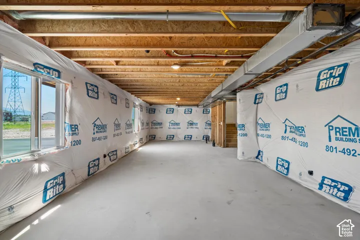 Unfinished lower level featuring exposed wood joists and subflooring, multiple windows, and a concrete floor