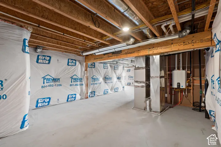 Unfinished basement featuring exposed wood joists, concrete flooring, and an on-demand water heater