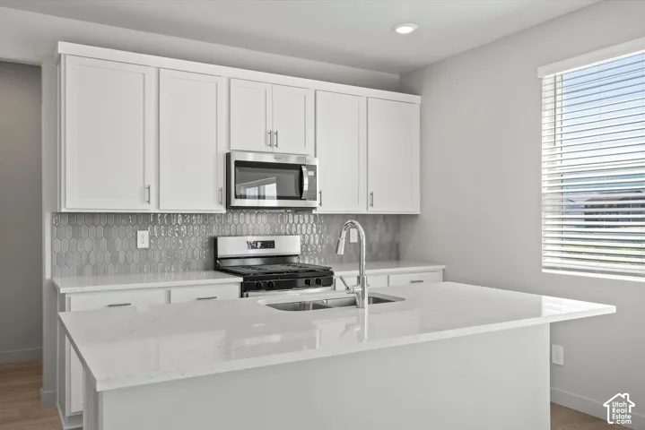 **DISLCAIMER**  Interiors do not show upgrades included. White shaker cabinetry, stainless steel appliances, modern gray picket tile backsplash, white countertops, and a kitchen island with an undermount sink