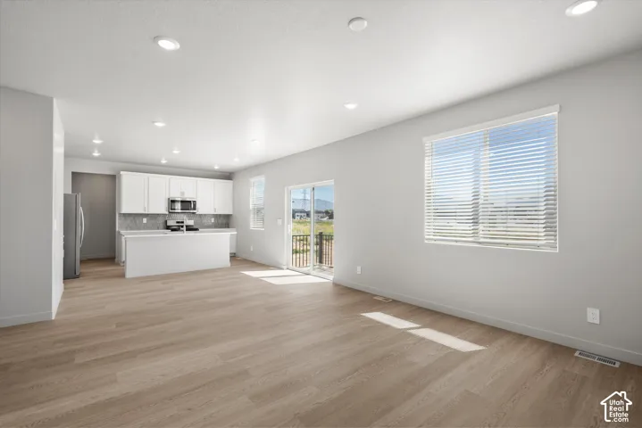 **DISLCAIMER**  Interiors do not show upgrades included. Open-concept living space featuring wood-finish flooring, recessed lighting, and a kitchen with white cabinetry and a tile backsplash