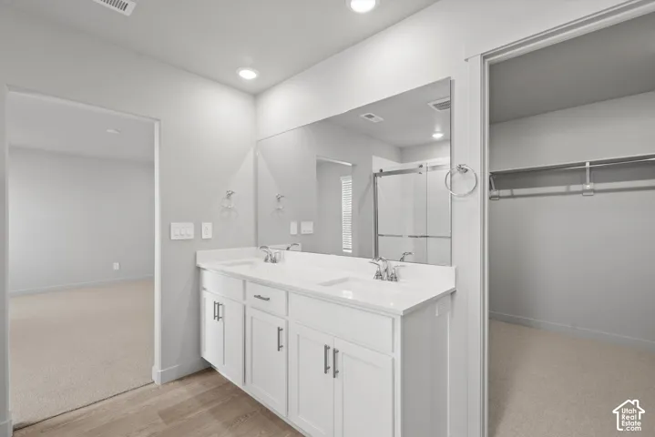 **DISLCAIMER**  Interiors do not show upgrades included. Dual vanity with white cabinetry and integrated sinks, a large wall-mounted mirror, recessed lighting, and wood-finish flooring