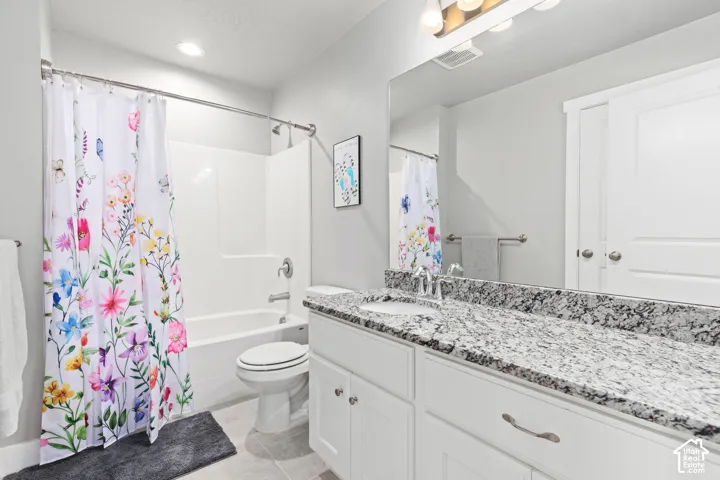 Bathroom featuring a built-in tub with shower, single vanity with a stone countertop, an integrated sink, and white cabinetry