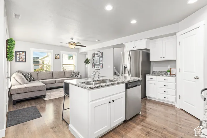 Open-concept living space featuring wood-finish flooring, recessed lighting, white cabinetry, stainless steel appliances, and granite countertops