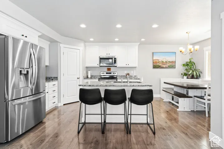 Kitchen featuring stainless steel appliances, white cabinetry, a central island with a granite-style countertop, recessed lighting, and wood-finish flooring