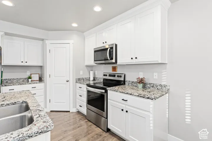 White shaker-style cabinetry, stainless steel appliances, granite countertops, wood-finish flooring, and recessed lighting