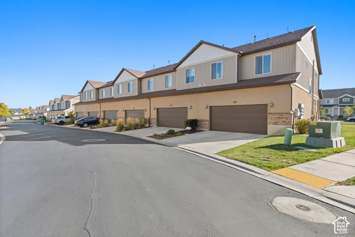 Townhome exterior featuring tan stucco, brown siding, a brown roof, and attached garages with brown doors