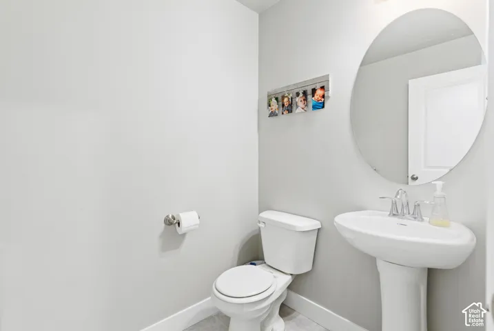 Pedestal sink with a chrome faucet, oval mirror, and white toilet
