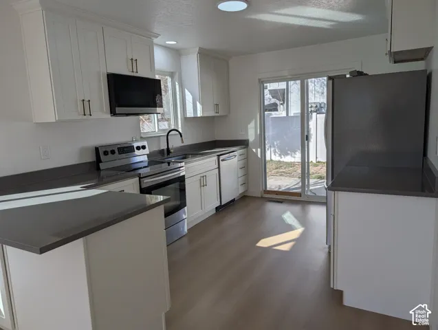Kitchen featuring white cabinetry, dark countertops, stainless steel appliances, wood-finish flooring, and a glass sliding door